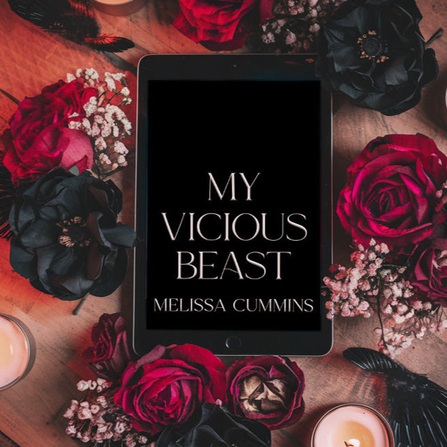 Tablet displaying 'My Vicious Beast' by Melissa Cummins surrounded by red and black roses and candles on a wooden surface.